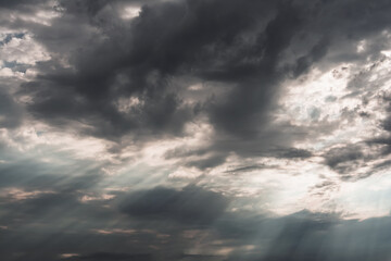 A view of a dark cumulus cloud in the sky through which the sun's rays break through.