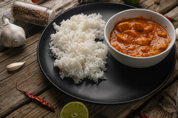Macro shot view of delicious chicken tikka masala curry and rice on rustic wooden table with spices background. Traditional Indian dish. Exotic tasty meal. Appetizing photo for menu or recipe