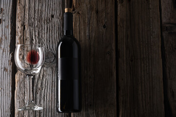 Elegant dark bottle and glass with remains of red wine on rustic wooden background. Advertising and...