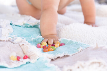 Obraz na płótnie Canvas Baby hand reaching out to grab colorful easter jelly beans on a light blue quilt