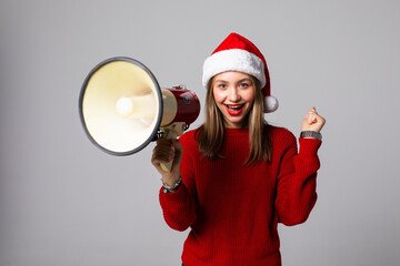 Excited young woman in santa hat holding megaphone over grey background
