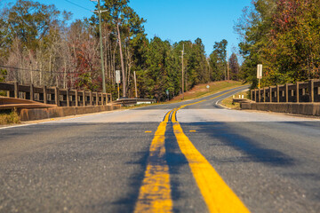 Fototapeta premium A road and bridge in the country with Fall colors and blue skies ground view
