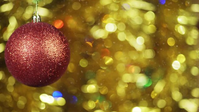 Red Christmas ball toy rotates clockwise on bokeh background of gold sparkles and lights.