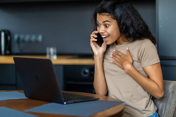 Pretty afro woman using smart phone and typing on laptop at home.