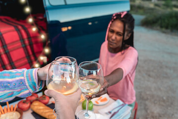 Multiracial friends cheering with white wine and celebrating outdoors in caravan - Focus on glasses