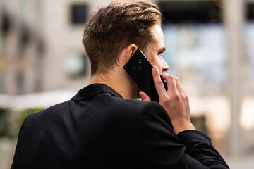 Young businessman talking on phone and walking in street. Unrecognizable man having business conversation during commuting to work. Back view