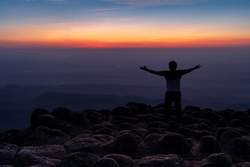 silhouette man in the back with arms open standing on viewpoint at nodular stones mountain peak or...