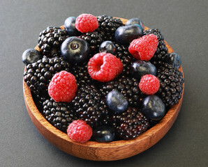 Fresh berries salad in a wooden plate on grey background.