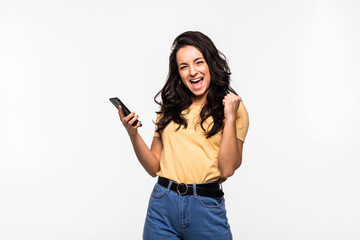 Portrait of a happy joyful woman holding mobile phone and celebrating a win isolated over white...