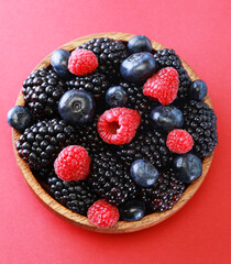 Fresh berries salad in a wooden plate on red background.