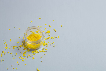 Transparent small jar with yellow pastry sprinkles on a gray background. Minimalistic banner with colors of the year 2021 - Illuminating and Ultimate Gray. - 398375668