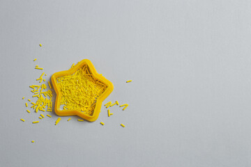 Yellow plastic cookie cutter filled with pastry sprinkles on a gray background. Minimalistic banner with colors of the year 2021 - Illuminating and Ultimate Gray. - 398375693