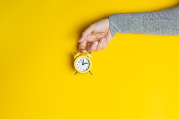 Female hand in gray clothes holding small alarm clock on yellow background. Creative banner with two colors of the year 2021 - Illuminating and Ultimate Gray - 398375825