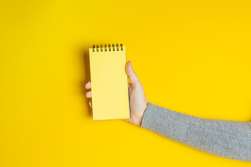 Female hand in gray clothes holding notepad with blank page on yellow background. Creative banner with two colors of the year 2021 - Illuminating and Ultimate Gray - 398375831
