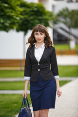 Young woman weared in classic business suit on background of a City park. Business style girl in Summer City on background of new park near a building. Street style Modern strict urban girl.