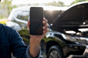 Male hand showing blank screen of smartphone. In front of broken down car. Emergency assistance service