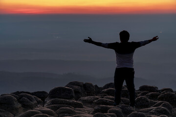 silhouette man in the back with arms open standing on viewpoint at nodular stones mountain peak or...