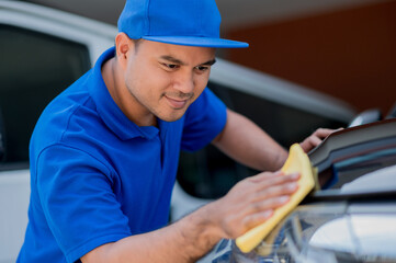 The car polisher uses a microfiber cloth and polish to wipe the car's headlamp or headlights to make them shine He takes care of every detail of the car.