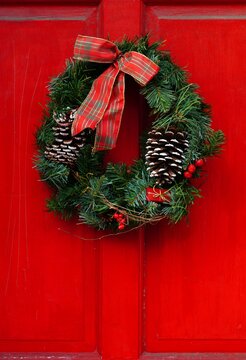 Christmas Holiday Pine Wreath With Pinecones And Red Bow On A Red Door