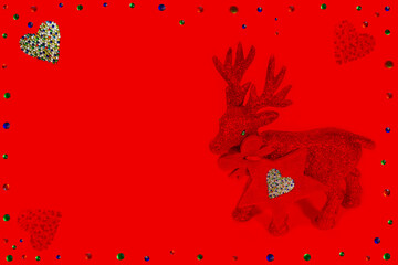Red reindeer figurine on a red background with hearts pattern. Frame from colorful crystals. Christmas background/card, gift card, Valentine's Day card, red star - pendant/tag. Copy space.