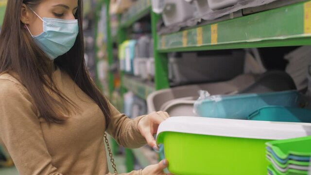 Young woman in face mask looks at green and white cat tray standing in local department store. Concept animal care service