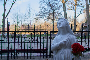 Statue of the Virgin Mary holding flowers with a fence and trees in the background