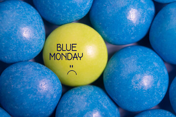Blue monday text with sad smiley face. One yellow candy in blue. Most depressing day of the year....