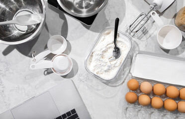 Top view of many culinary pieces of equipment for a homemade healthy cuisine. Ingredients prepared on the white and clean marble countertop, Laptop opening ready for online learning at home