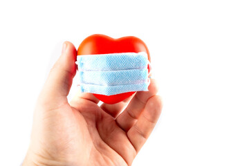 red heart in hands in a medical mask on a white background