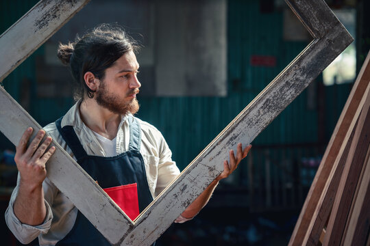 carpenter in wood workshop selecting wooden frame for his workwood