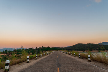Asphalt road through the grass field and reservoir in the morning time.