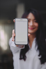 young attractive Asian woman showing her smartphone with white screen to the camera in a coffee shop mockup phone screen