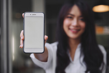 young attractive Asian woman showing her smartphone with white screen to the camera in a coffee shop mockup phone screen