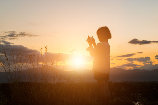 Silhouette of child girl holding a smartphone taking pictures at meadow on sunset time.