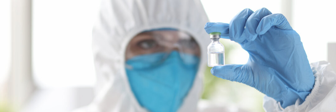 Researcher in protective suit looks at medicine bottle.