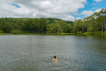 Obraz na płótnie Canvas Young lady swimming in a small lake surrounded by green land and wood forest.. Monte Alegre Do Sul, Brazil. 