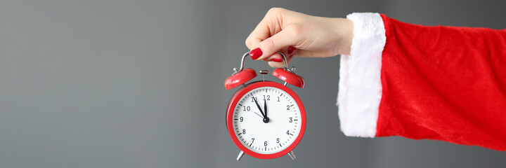 Hand in santa claus costume holds red alarm clock.