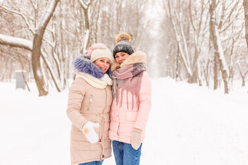 Fototapeta na wymiar Two girls are walking in a winter park in the snow. Sisters on the background of snowy trees