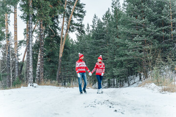 A guy with a girl in red knitted sweaters go to the help in the winter forest.