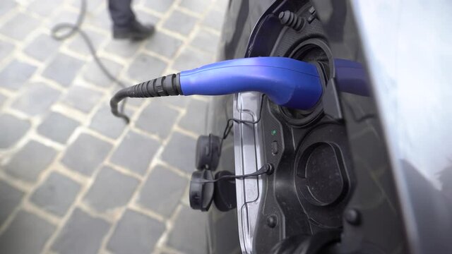Modern businessman charges her electric car in the city.