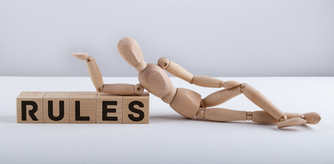 The wooden man lies near the wooden cubes with the text RULES. Business concept.