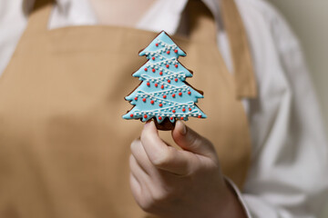 The pastry chef holds a gingerbread in the shape of a Christmas tree. The symbol of the new year and merry christmas.