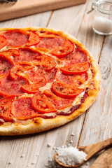 Closeup on ham pizza with tomato with dried herbs on the wooden table