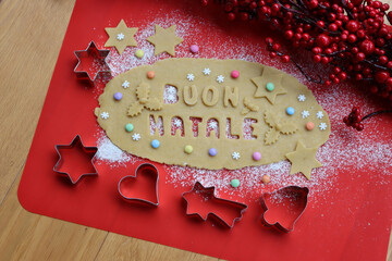 Buon Natale.Cookie dough letters on wooden table with sugar snowflakes and colorful chocolate...