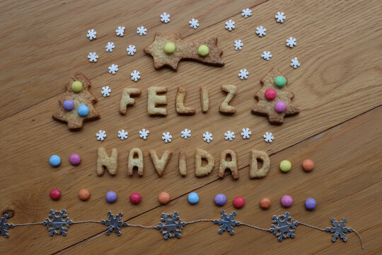 Feliz Navidad. Baked cookie letters on wooden table with sugar snowflakes and colorful chocolate candies