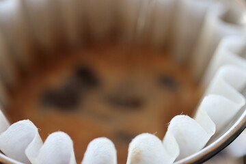 Barista making coffee with a pour over coffee maker in a dripper and pouring hot water from a black pot on a macro scale