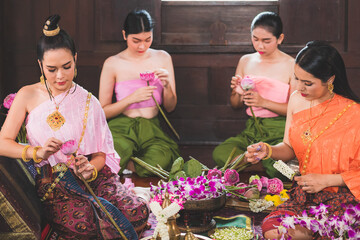 Obraz premium A beautiful Thai woman and she wears traditional Thai costumes, both masters and servants They are sitting preparing flowers in a wooden house to make merit on the day of the Buddha.