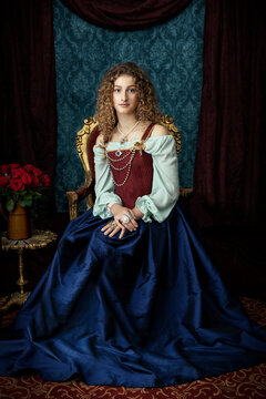 A young renaissance woman sitting in a gold and red velvet chair