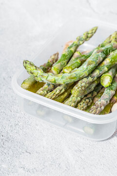 frozen green asparagus pods in a clear white container. on texture. light background. copyspace