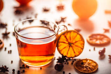 Glass cup of hot aromatic tea on white background with spices. Christmas tea with oranges on bokeh lights background. Christmas tea.
